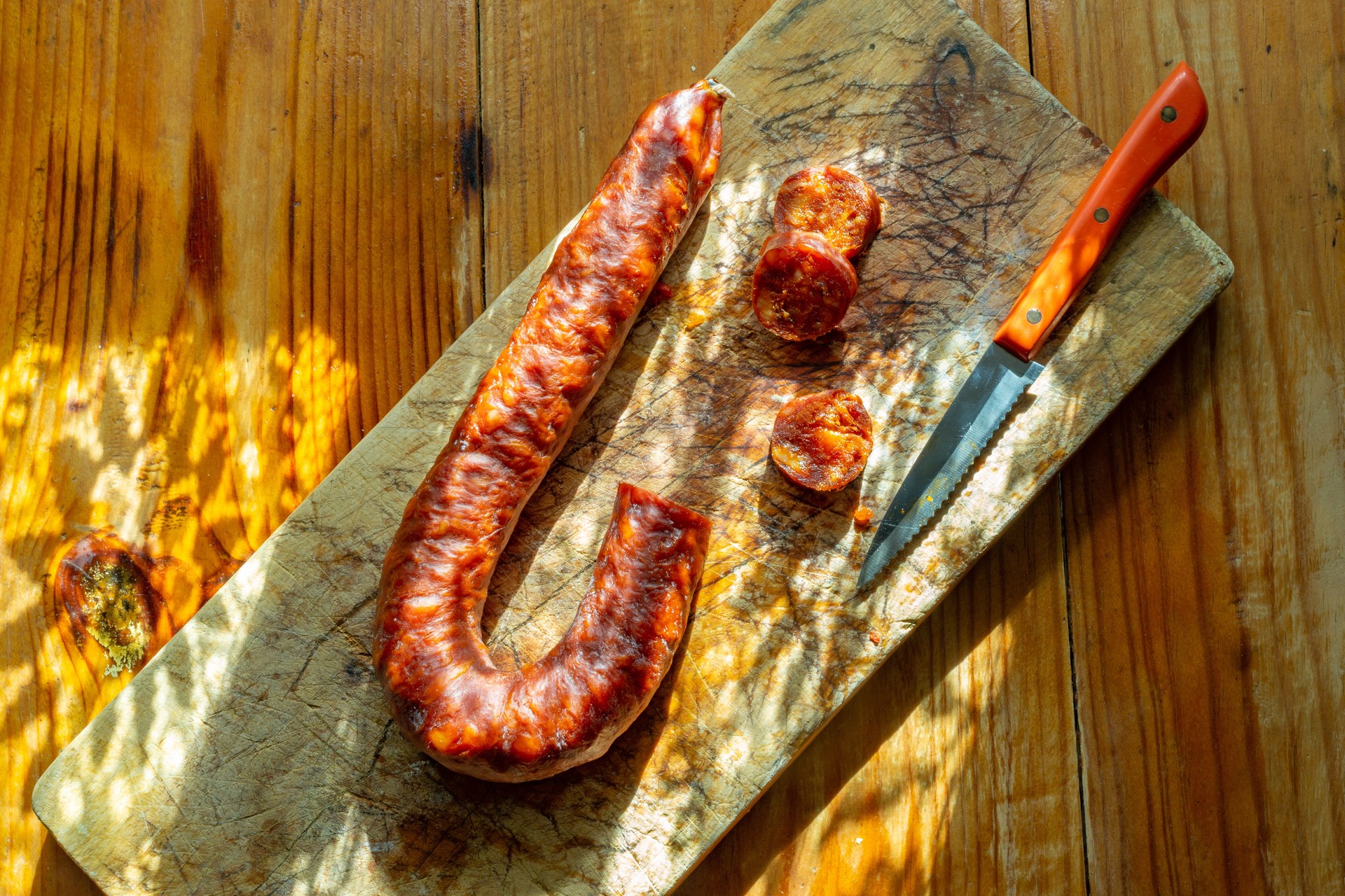 Salchicha y cuchillo en una tabla de cortar de madera sobre la mesa.